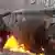 Демонстрант перед сгоревшим автобусом бросает дымовую шашку
