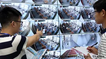 Chinese invigilators check a big screen showing live footages from surveillance cameras in classrooms