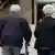 An elderly man and woman seen from behind walking down a street