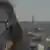 Hava kirliliğinden dolayı filtreli maske takmış olan bir kişi, arka planda kent görüntüsü