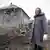 Жительница Донбасса на фоне разрушенного войной дома 