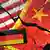 Mão segura celular com as cores da bandeira alemã, ao fundo bandeira dos EUA e China rachadas