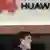Homem fala ao celular diante da logomarca da Huawei no escritório da empresa em São Paulo