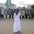 Женщина в белом платье стоит одна перед шеренгой омоновцев в касках и со щитами 