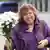 Belarusian writer and journalist Svetlana Alexievich holds a bunch of white flowers. She is wearing a purple coat and has a large smile.