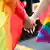 Two hands entwined, surrounded by rainbow flags