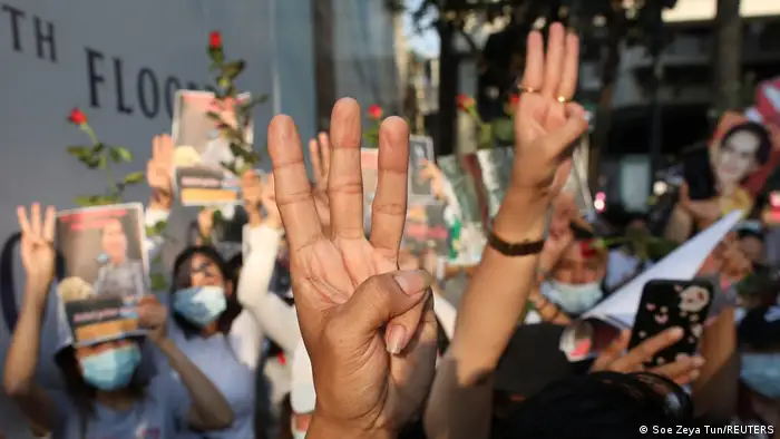 Dozens of protesters hold their hands up in a three-finger salute in February 2021