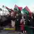 A Libyan family waves national flags in front of a celebrating crowd on the anniversary of the revolution.