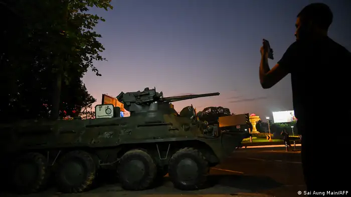 A man takes a photo of a tank as it drives down a darkened city street