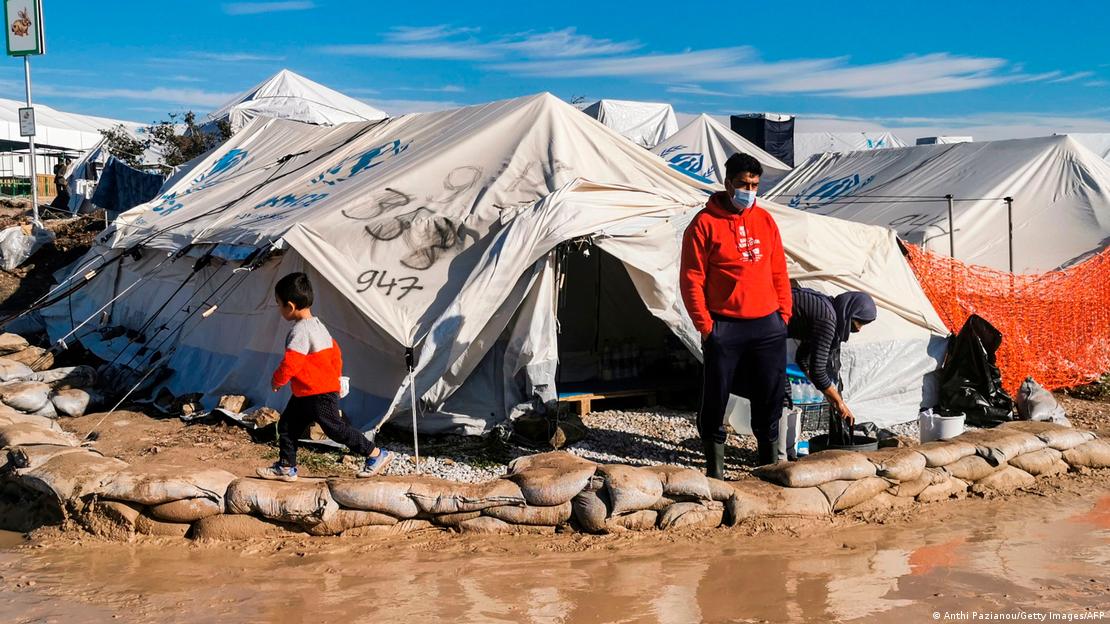 Yunanistan'ın Midilli Adası'ndaki Kara Tepe Sığınmacı Kampı'nda, içeri su girmesin diye etrafı kum çuvalları ile çevrilmiş olan bir çadır ve çadırın önünde iki yetişkin ve bir çocuk - (19.12.2020)