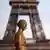 A picture taken on May 2, 2020 shows a bronze statue wearing a face mask, with the Eiffel Tower in the background