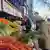 Havuç, pırasa ve meyvelerin olduğu bir pazar tezgahı önünde bir kadın alışveriş yapıyor