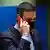 Spanish Prime Minister Pedro Sanchez speaks on a phone with a red case while wearing a black facemask