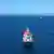 Sembol fotoğraf - Açık denizde yük taşıyan bir gemi ve uzakta birkaç yelkenli