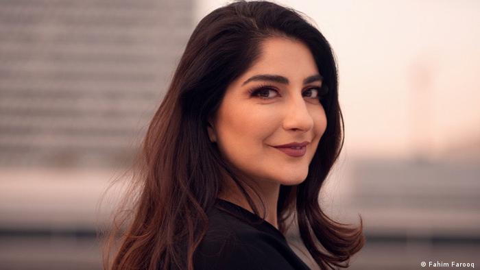 Portrait of DW Waslat Hasrat-Nazimi. She is standing sideways while looking and smiling directly at the camera. Her long dark hair is loose and she wears dark brown lipstick. 