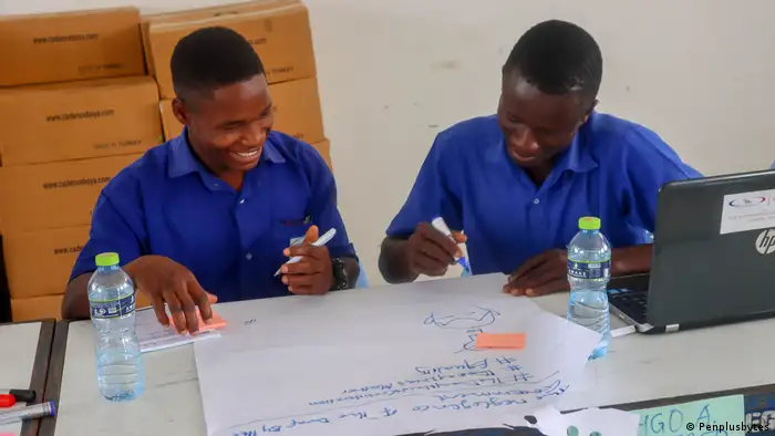 Zwei Schüler der House of Grace School for the Deaf in Ghana sitzen am Tisch und schreiben in einer Gruppenarbeit auf ein großes Blatt Papier. 