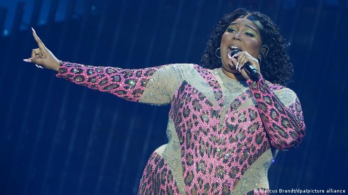 Lizzo singing on a stage in a leopard print jumpsuit.