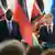 Zwei Männer in Anzügen stehen vor zwei Rednerpulten. Hinter ihnen stehen verschiedene Flaggen in bunten Farben, die rechte Flagge trägt Sterne. 
