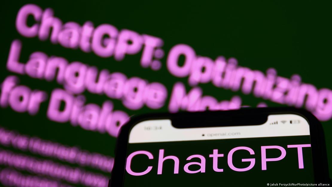 Ön planda bir akıllı telefonun ekranında, arka planda bir ekranda ChatGPT yazıları