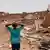 Un jeune garçon vu de dos croise ses mains sur sa tête en contemplant les ruines d'une maison à Khartoum (photo du 25 avril 2023)