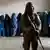 A Taliban fighter stands guard as women wait to receive food rations distributed by a humanitarian aid group, in Kabul