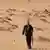 A man walks toward livestock in the Saudi desert. 