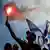 A protester holds up a torch with Israeli flags in the background