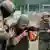 Two fighters in military gear at a shooting range, one pointing a gun while the other corrects his posture