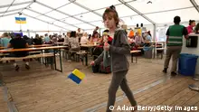 A child refugee from Ukraine holds a Ukrainian flag as she walks through a temporary welcome center tent outside the main train station in Berlin