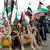 Huthi Rebellen in Militäruniform sitzen vor palästinensischen Flaggen