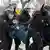 Cinco policiais de negro e com capacete com viseira carregam homem em paisagem de neve