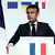 Emmanuel Macron, in a dark suit, standing at a podium surrounded by French, EU, Ukrainian and other flags.
