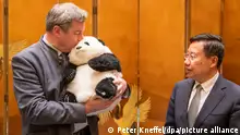 25.03.2024, China, Chengdu: Markus Söder, (l, CSU) Ministerpräsident von Bayern, hält einen Pandabären aus Plüsch in den Armen, den er zuvor von Wang Xiaohui (r), Parteisekretär der Kommunistischen Partei, als Gastgeschenk überreicht bekommen hat. Söder bereist bis zum 28.03.2024 die Volksrepublik China. Foto: Peter Kneffel/dpa +++ dpa-Bildfunk +++